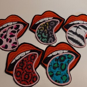 Könnte beinhalten: Fünf gestickte Aufnäher in Form von offenen Mündern mit roten Lippen und weißen Zähnen. Jede Zunge zeigt ein anderes Muster: rosa Leopardenmuster, blaugrünes und schwarzes Leopardenmuster, schwarz-weiße Zebrastreifen, rote Kreise und blaues Leopardenmuster.