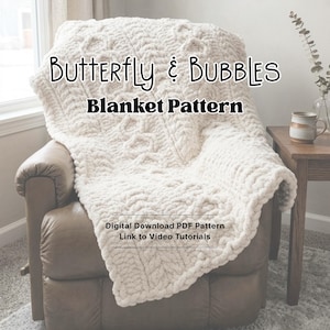 Op de afbeelding: Een crèmekleurige, getextureerde deken gedrapeerd over een bruine leren stoel. De deken heeft een kabelgebreid ontwerp met de woorden "Butterfly & Bubbles Blanket Pattern" in zwarte tekst. Extra tekst geeft een digitaal PDF-patroon met video tutorials aan.