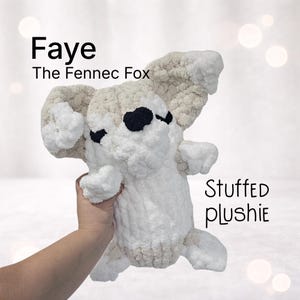 May include: A handmade stuffed plushie of a Fennec Fox named Faye. The plush toy is white and tan with black accents. The text "Faye The Fennec Fox" and "Stuffed plushie" are written on the image.