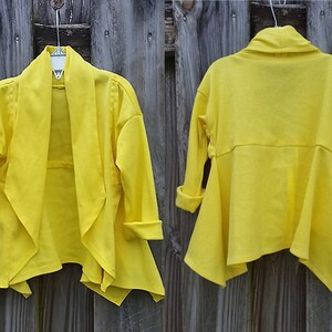 May include: A bright yellow cardigan with a draped front and long sleeves. The cardigan is made of a soft, lightweight fabric and has a relaxed fit.