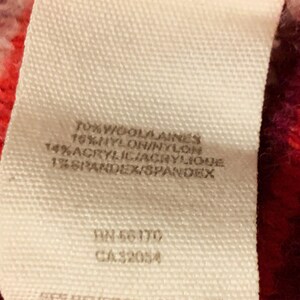 Może przedstawiać: Biała metka z czarnym tekstem, na kt&oacute;rej wymieniono skład tkaniny swetra. Metka zawiera: 70% Wełna/Laines, 16% Nylon/Nylon, 14% Akryl/Acrylique, 1% Elastan/Spandex. Metka zawiera r&oacute;wnież numery: RN 56170 i CA 32054.