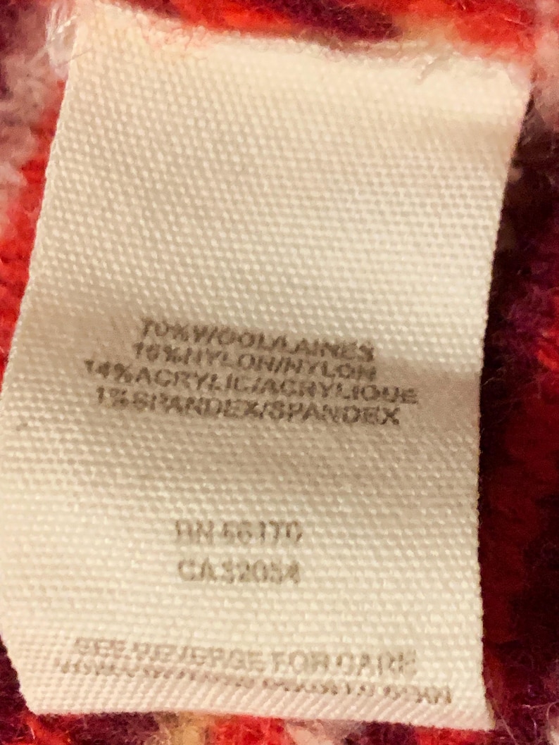 Może przedstawiać: Biała metka z czarnym tekstem, na kt&oacute;rej wymieniono skład tkaniny swetra. Metka zawiera: 70% Wełna/Laines, 16% Nylon/Nylon, 14% Akryl/Acrylique, 1% Elastan/Spandex. Metka zawiera r&oacute;wnież numery: RN 56170 i CA 32054.