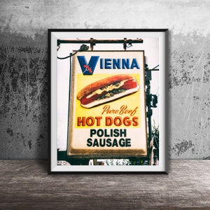 May include: A vintage sign with a red and white "V" for Vienna, advertising "Pure Beef Hot Dogs" and "Polish Sausage". The sign features a yellow background with red and black text and a photo of a hot dog with mustard and relish.