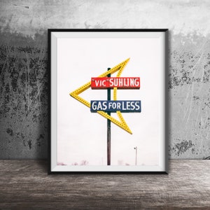 Puede incluir: Un letrero de gasolinera vintage con una flecha amarilla apuntando hacia la derecha. El letrero dice "Vic Suhling Gas for Less" en letras rojas, azules y amarillas.