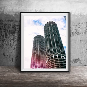 May include: A framed photograph of two tall, modern buildings with a cloudy sky in the background. The buildings are made of concrete and have a grid-like pattern. The photograph is in a black frame.