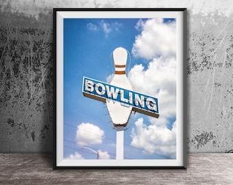 May include: A framed wall art print featuring a vintage-style bowling sign. The sign is shaped like a white bowling pin with orange stripes and a blue rectangular banner across the center with the word BOWLING in white capital letters.