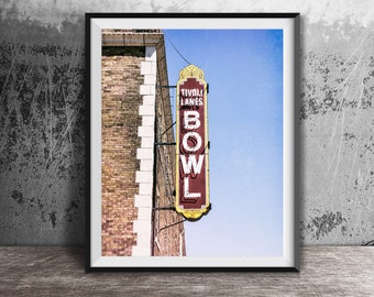 May include: A vintage sign for Tivoli Lanes Bowl, a bowling alley. The sign is red with white lettering and a yellow border. It is mounted on the side of a brick building.