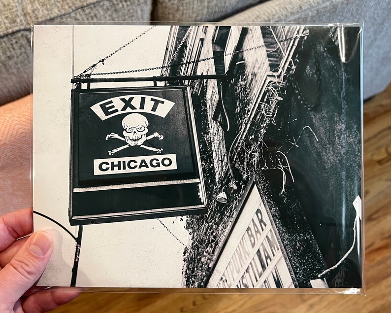Op de afbeelding: Zwart-witfoto van een bord met een schedel en gekruiste beenderen en de woorden "Exit Chicago".