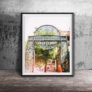 May include: A framed photograph of a decorative metal archway with the words "Old Town" inscribed on it. The archway is located in a city street with trees and buildings in the background.