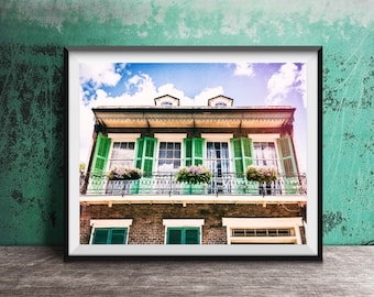 May include: A framed photograph of a brick building with green shutters and a balcony. The building has a white trim and a blue sky is visible in the background.