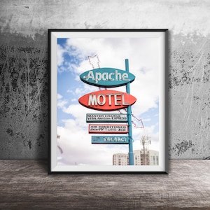 Peut inclure: Impression encadrée d'un panneau de motel vintage. Le panneau affiche "Apache Motel" en rouge et bleu, avec du texte supplémentaire indiquant les équipements. Le ciel est bleu avec des nuages duveteux, et le panneau est monté sur un poteau.