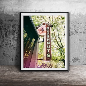 May include: A vintage sign for a shop called "Top Pot Doughnuts" hangs outside a building. The sign is red and white with green lettering and a picture of a horse on it. The sign is surrounded by green trees.