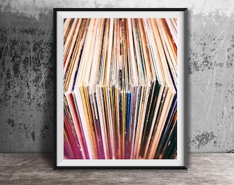May include: A framed wall art print featuring a vertical, high-angle perspective of a dense collection of vinyl record sleeves. The image displays a spectrum of colorful spines arranged in a row, creating a textured, linear pattern within a black frame.