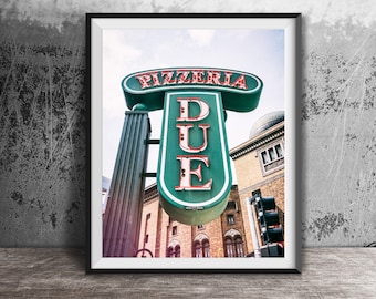 May include: A framed wall art print featuring a vintage-style green and white neon sign that reads PIZZERIA DUE in bold red and white lettering. The sign is mounted on a dark green pillar against a brick building with arched windows and a dome.