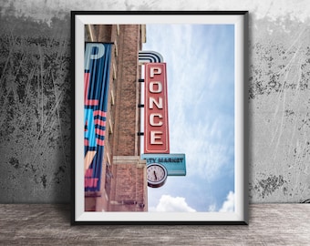 May include: A framed photograph of a brick building exterior featuring a vertical red sign with the white text PONCE, a blue sign with the text CITY MARKET, and a round analog clock face. A blue banner with partial text hangs on the left side.