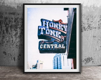 Może przedstawiać: Zdj?cie w ramie neonowego szyldu z napisem "Honky Tonk Central" w stylu vintage. Szyld jest zamontowany na ceglanym budynku z białym niebem w tle.