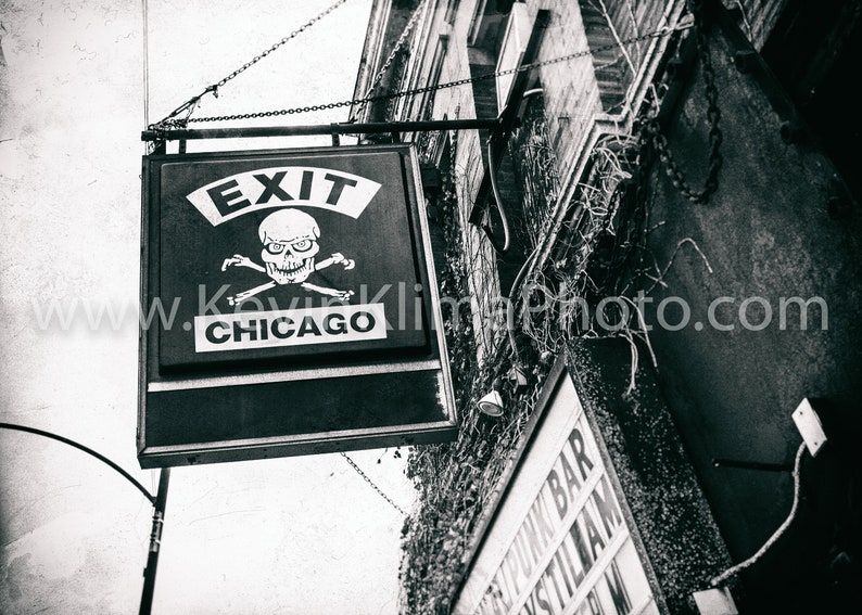 Op de afbeelding: Zwart-wit bord met de woorden "Exit Chicago" en een schedel met gekruiste beenderen.