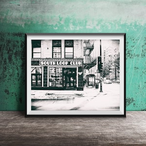 May include: Black and white photograph of a building with a sign that reads "South Loop Club". The building has a fire escape and is located on a city street.