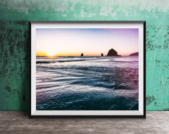May include: A framed photograph of a seascape with a rocky island in the distance. The sky is a vibrant purple and orange, and the water is a deep blue. The sun is setting behind the island, casting a warm glow on the water.