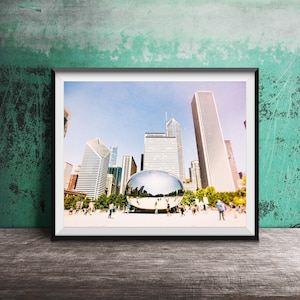 May include: A framed photograph of the Chicago skyline with the Cloud Gate sculpture in the foreground. The photo is taken from a low angle, looking up at the skyscrapers. The sky is blue and there are clouds in the background.