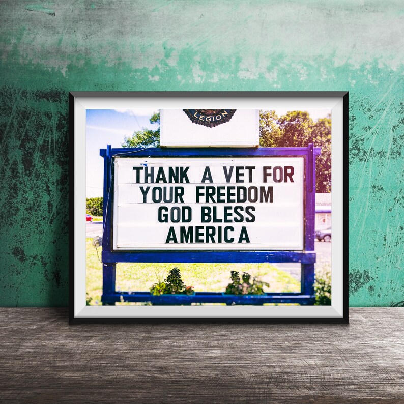 May include: Framed sign with the text "THANK A VET FOR YOUR FREEDOM GOD BLESS AMERICA." The sign is white with black lettering and is set against a blue frame. The word "LEGION" is at the top of the sign.
