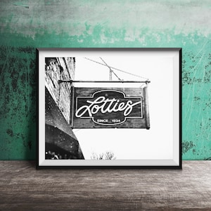 Pode incluir: Fotografia a preto e branco de uma placa pendurada num edif&iacute;cio que diz "Lotties Since 1934".