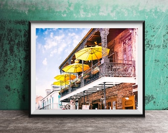 May include: A photograph of a building with a balcony and yellow umbrellas. The building is made of brick and has a wrought iron railing. The umbrellas are hanging from the balcony and are casting shadows on the building.