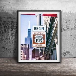 Puede incluir: Un cartel vintage con el texto "BEGIN HISTORIC ILLINOIS U.S. 66 ROUTE" en rojo, blanco y azul. El cartel está montado en un poste frente a un edificio alto.