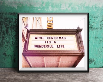 May include: A framed wall art print featuring a vintage theater marquee with black lettering on a white background that reads WHITE CHRISTMAS ITS A WONDERFUL LIFE. The marquee has a dark brown frame and is mounted on a textured wall surface.