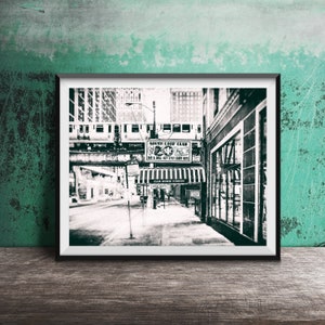 Op de afbeelding: Zwart-witfoto van een straat in de stad met een treinspoor erboven. Het bord voor "South Loop Club" is zichtbaar op de voorgrond. De foto heeft een vintage, korrelige uitstraling.