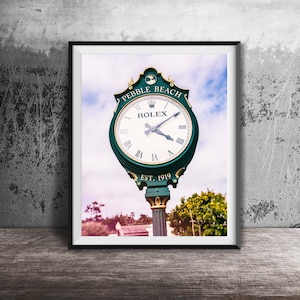 May include: A framed wall art print featuring a green and gold outdoor clock with a white face, Roman numerals, and the text Pebble Beach, Rolex, and Est. 1919. The clock is mounted on a post against a sky background with trees visible below.