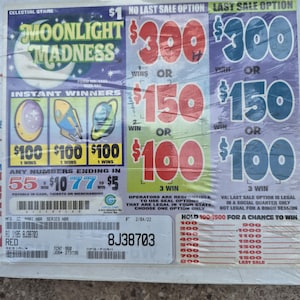 Może przedstawiać: Karta do gry Moonlight Madness z grafiką półksiężyca, kwotami wygranych natychmiastowych 100$, 150$ i 300$ oraz listą liczb kończących się na 55 lub 77 dla wygranych 5$ i 10$. Karta zawiera kody kreskowe oraz numer seryjny 8J38703.