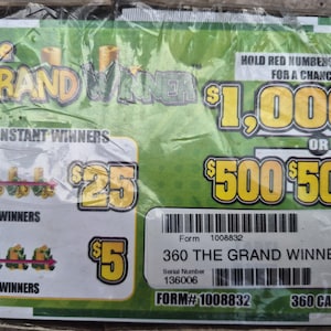 May include: A green rectangular lottery game card titled The Grand Winner with yellow text displaying prize amounts of $1,000, $500, $25, and $5. The card features a barcode, form number 1008832, serial number 136006, and instructions to hold red numbers 013-3513.