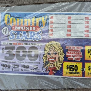 Op de afbeelding: Een Country Music Stars lot in doorzichtig plastic verpakt. Het lot bevat een cartoonillustratie van een blonde vrouw met een microfoon, met tekst waaronder een totale waarde van $300 en instructies voor het spel.
