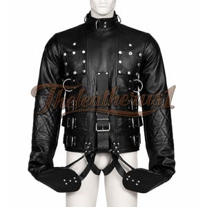 May include: A black leather jacket featuring a high collar with a metal D-ring, silver-toned studs, and multiple adjustable buckled straps across the front. The long sleeves have quilted detailing, and integrated straps extend downward to secure the cuffs.