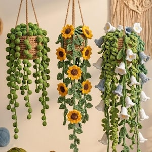 Peut inclure: Trois décorations de plantes en crochet suspendues dans des paniers tressés. La gauche présente des vignes perlées vertes, le centre affiche des tournesols jaunes avec des feuilles vertes, et la droite montre des vignes vertes avec des fleurs en cloche.