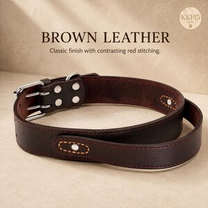 May include: A brown leather collar featuring contrasting red stitching, a silver-toned metal buckle, and silver rivets. The text "BROWN LEATHER" and "Classic finish with contrasting red stitching." is visible, along with a circular "KKP15" logo.