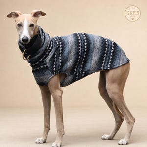 Könnte beinhalten: Ein rehfarbener Whippet trägt einen Hundepullover mit hohem Kragen und einem geometrischen Dreiecksmuster in Dunkelblau, Grau und Weiß. Der Hund trägt ein schwarzes Halsband mit einem goldenen D-Ring aus Metall. Ein kreisförmiges Logo zeigt KKP15.