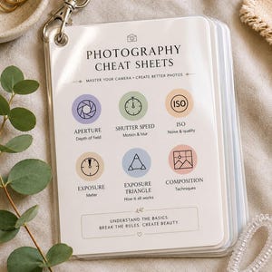 以下が含まれることがあります： リング付きのラミネート加工された写真撮影用チートシートセット。ベージュのストラップが付いています。表紙には「Photography Cheat Sheets」という文字と、絞り、シャッタースピード、ISO、露出、露出の三角形、構図テクニックのアイコンが印刷されています。