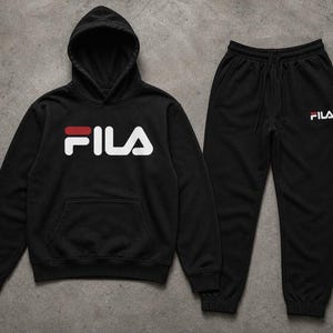 May include: A black hooded sweatshirt and matching black sweatpants set. The hoodie features a large white and red FILA logo on the chest. The sweatpants have a smaller white and red FILA logo on the upper left thigh and include a drawstring waist.