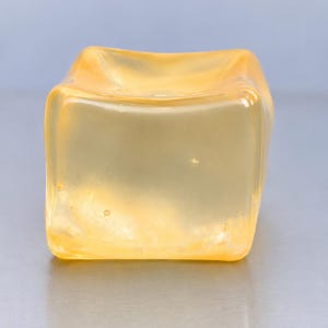Op de afbeelding: Een doorschijnende, lichtgele kubus met afgeronde randen en een glad, glanzend oppervlak. Het object heeft een zacht, geleiachtig uiterlijk met subtiele interne variaties in kleurdichtheid, wat een lichtreflecterend effect op de vorm cre&euml;ert.