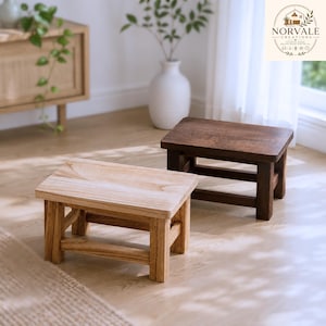 May include: Two small wooden stools with rectangular tops and four legs connected by horizontal support bars. One stool features a light natural wood finish, while the other stool is finished in a dark brown stain. Both stools have a simple design.