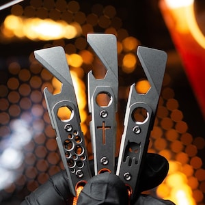 May include: Three silver multi-tools with different designs. The tools have a bottle opener, a flathead screwdriver, and a Phillips head screwdriver. The tools are attached to orange lanyards.
