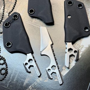 May include: Two silver-colored metal multi-tool knives with Amsler branding, each featuring a sharp blade, hexagonal cutouts, and a bottle opener. Two black textured sheaths are included, one with a long silver ball chain attached to it.