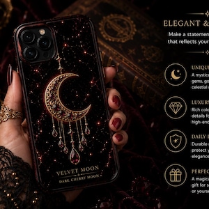 May include: A black smartphone case featuring a gold crescent moon design with dangling red gemstone-like accents. The case displays the text VELVET MOON and DARK CHERRY MOON at the bottom. The background includes text about the product features.