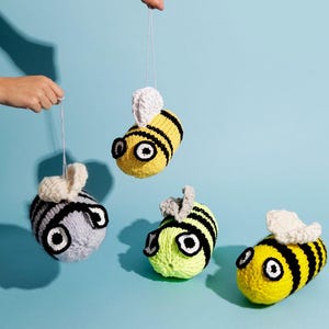 Puede incluir: Cuatro adornos de abeja tejidos a ganchillo con cuerpos redondos, rayas negras y alas blancas. Una abeja es gris claro, una es amarillo neón y dos son amarillo brillante. Cada abeja tiene grandes ojos circulares blancos y negros y un hilo.