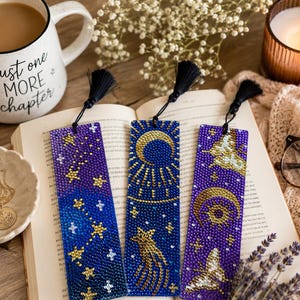May include: Three rectangular bookmarks featuring diamond art designs in shades of blue and purple. The left bookmark shows constellations, the center features a crescent moon and shooting star, and the right displays a moon and moth, each with a black tassel.