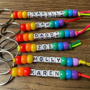 Può includere: Sei portachiavi personalizzati con perline quadrate bianche e lettere nere che compongono i nomi ISABELLA, SAM, DADDY, ZOE, MOLLY e KAREN. Ogni portachiavi include un anello in metallo e una sequenza di perline in plastica rossa, arancione, gialla, verde, blu e viola.