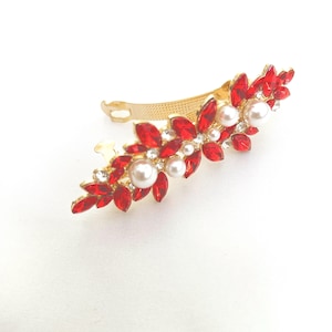 May include: A gold-toned hair clip featuring a decorative arrangement of marquise-cut red crystals, small clear rhinestones, and round white faux pearls. The metal base has a textured finish and a hinged mechanism for securing hair in place.