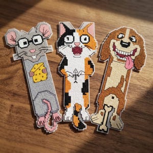 Peut inclure: Trois marque-pages en point de croix représentant des animaux de dessin animé. À gauche, une souris grise à lunettes tenant un fromage jaune. Au centre, un chat calico tenant une arête de poisson. À droite, un chien beagle brun et blanc avec un os.